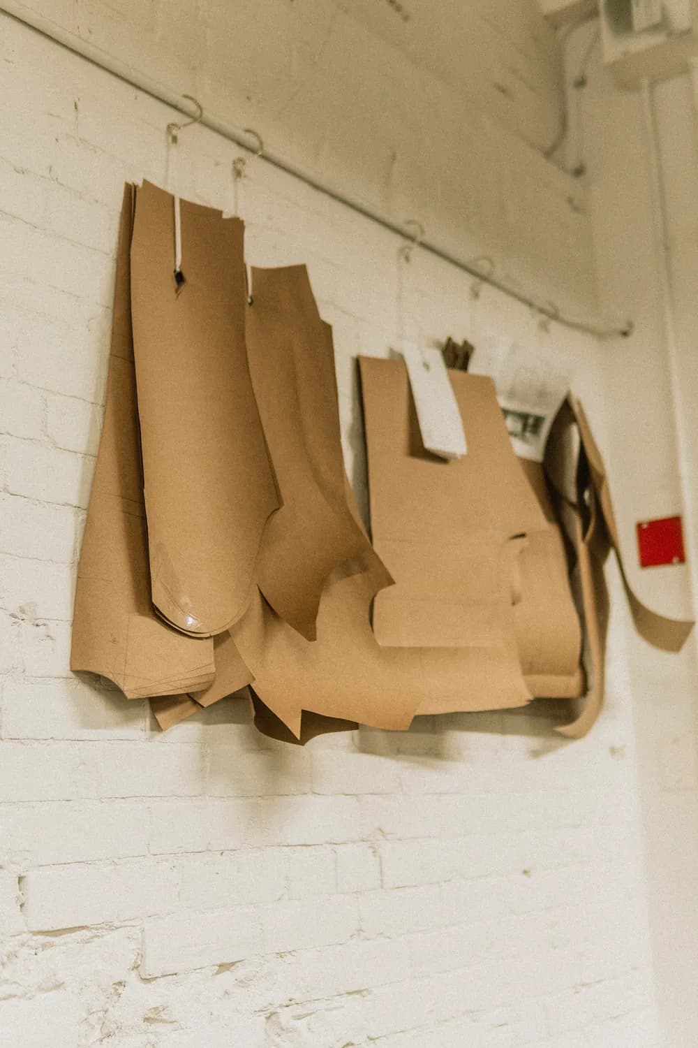 Individual paper tailoring patterns hanging against the atelier’s brick wall